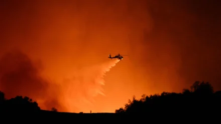 Un helicóptero arroja agua sobre el humo y las llamas del incendio Palisades que arde detrás de Mulholland Drive hacia el vecindario de Encino en los Ángeles, California